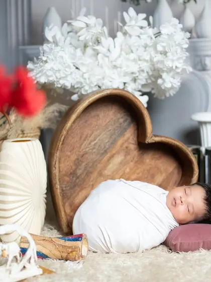 A beautifully composed shot of a swaddled newborn, with red flowers adding a pop of color to the foreground.