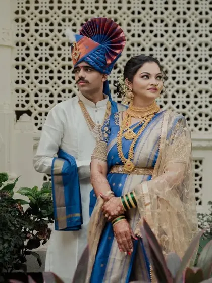 A regal portrait of a couple in royal blue and white Maharashtrian attire.