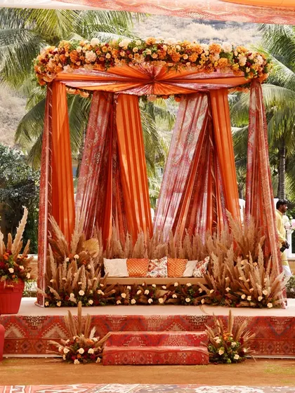 The couple's seating at the Souk Bazaar Mehndi, framed by rich orange drapes and rustic pampas grass. The design perfectly blends traditional colors with bohemian elements for a unique look.