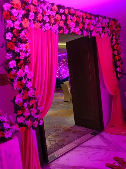 I can transform any doorway into a beautiful photo opportunity. Here, an indoor entrance is decorated with an arch of pink and orange flowers, enhanced by dramatic pink lighting to match the event's theme.