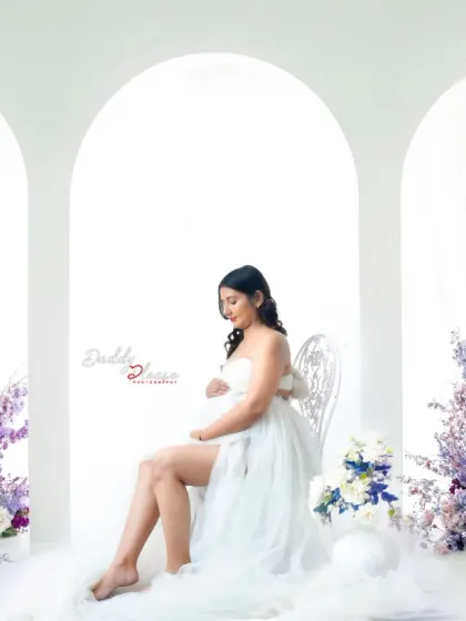 The color version of my angelic setup, featuring a mom-to-be in a white outfit with wings, surrounded by soft clouds and beautiful purple flowers.