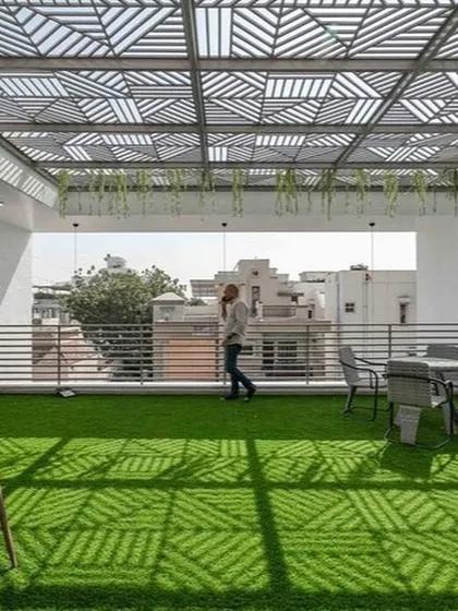 This rooftop terrace uses a stunning geometric-patterned pergola to create a dynamic play of light and shadow on the artificial turf below. It's a modern, spacious, and visually striking design perfect for gatherings.