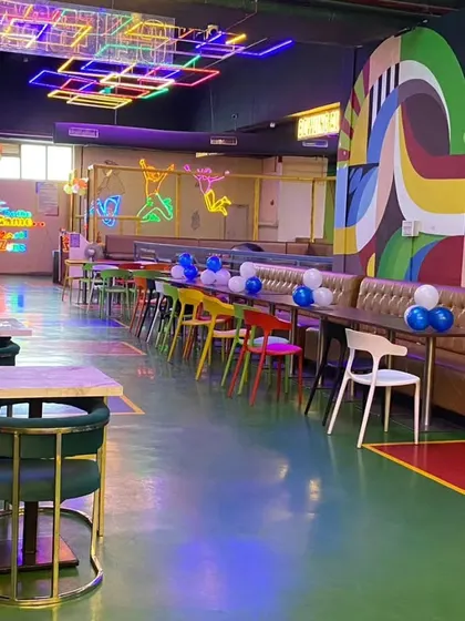 A wide view of a large, colorful cafe space prepared for a birthday party. Simple balloon bunches on the tables add a pop of color throughout the venue.