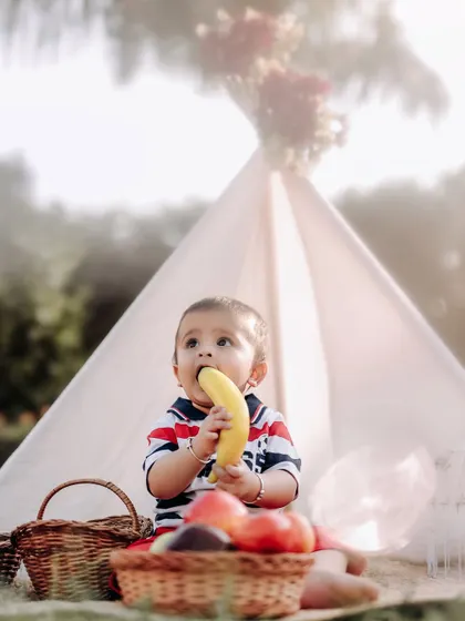 A healthy snack during a fun outdoor photoshoot. This little one is enjoying a banana at his picnic, a real and adorable moment captured on camera.