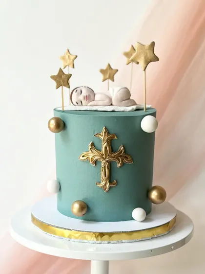 A sophisticated baptism or christening cake in a deep teal. The cake is decorated with a sleeping baby topper, stars, and an ornate golden cross.