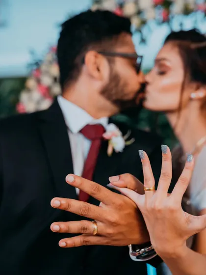A close-up shot focusing on the couple's hands and rings, with a romantic kiss blurred in the background, symbolizing their new union.