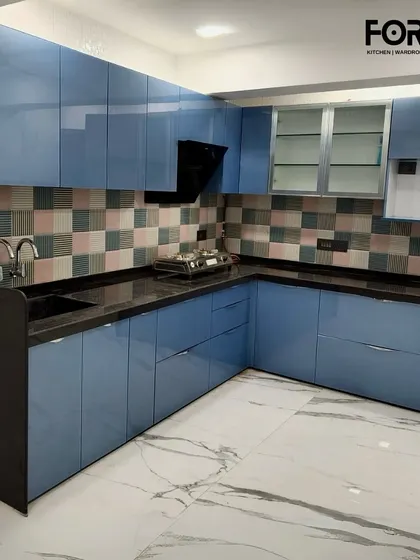This L-shaped kitchen features vibrant blue acrylic cabinets and a patterned tile backsplash. The black countertop provides a grounding contrast, showcasing our ability to work with bold colors to create a personalized space.