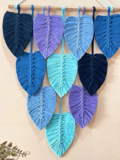 A close-up of the blue and purple leaf wall hanging. You can see the detailed knotting that forms the spine of each leaf and the soft, brushed-out texture of the cord.