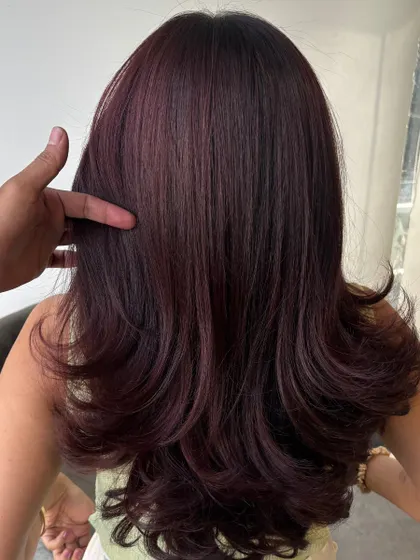 A stylist's hand showcases the texture and color of the burgundy waves, highlighting the quality of the work.
