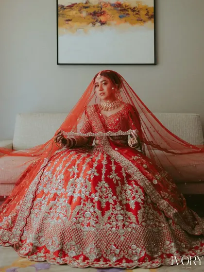 A classic bridal portrait. The bride, seated and draped in her magnificent red lehenga, looks every bit the part of a traditional, royal bride.