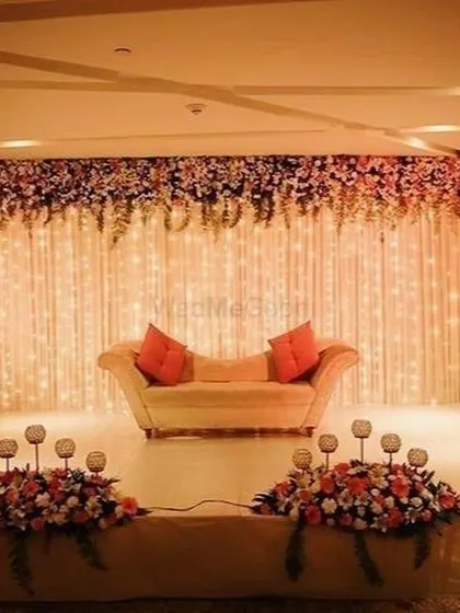 A curtain of warm fairy lights creates a magical and romantic backdrop for this reception stage. The simple sofa with bright cushions provides a pop of color, while the overhead floral runner adds a touch of natural beauty to the entire setup.