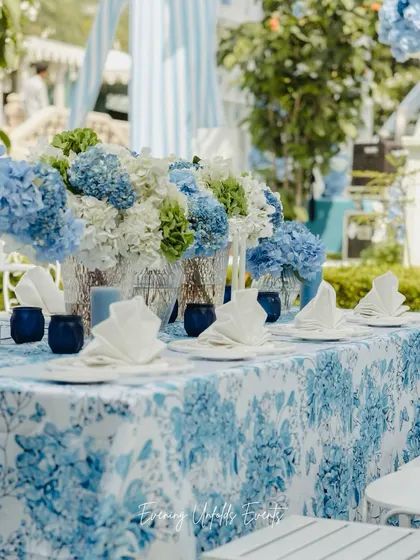 A close-up of the tablescape from the Dior-inspired Mehendi at Raffles Udaipur. The custom-printed tablecloth, blue glassware, and arrangements of blue and white hydrangeas create a cohesive and elegant look.