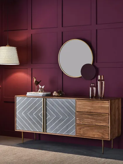 This shot focuses on a modern sideboard against a rich, jewel-toned wall. The composition highlights the furniture's clean lines and mixed materials, while the styling adds a touch of personality and context.