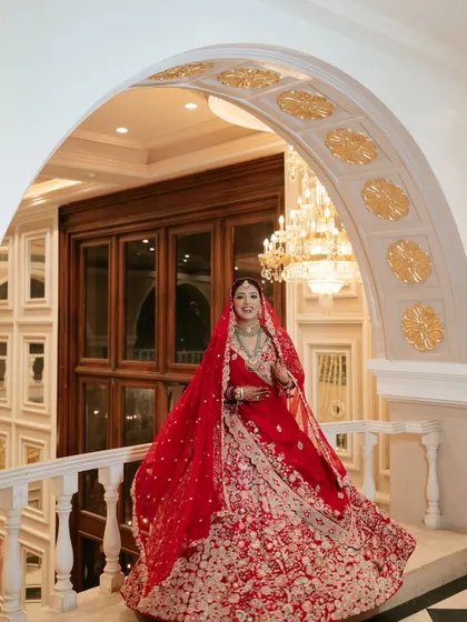 A full-length view of this magnificent bridal look. The grand setting and her stunning red lehenga called for makeup that was both classic and striking, ensuring she was the center of attention.