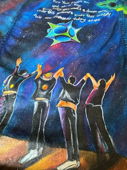 A detail shot from the back of the black Coldplay jacket, focusing on the painted figures and the galaxy art. This design includes lyrics from "Adventure of a Lifetime" and "Diamonds."