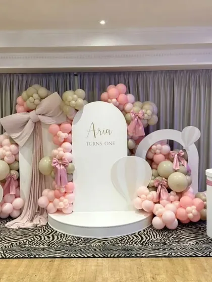 A beautiful Western-style setup for Aria's first birthday, featuring soft pink and beige balloons, elegant bows, and hot air balloon props on a zebra-print floor for a trendy contrast.