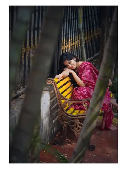 A quiet, contemplative moment on a park bench. The framing through the trees adds a sense of intimacy to this beautiful saree portrait.