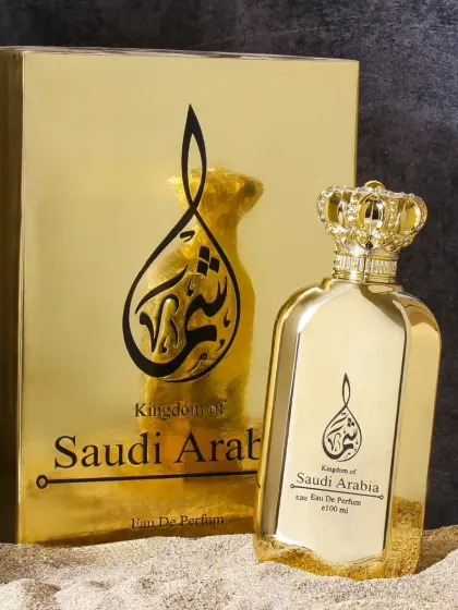 This opulent photo showcases a gold perfume bottle shaped like a crown, complete with its gold packaging. The sandy base adds a touch of Arabian desert mystique, enhancing its regal theme.