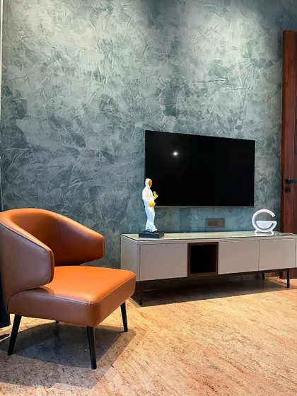 Another view of the bedroom lounge corner in Ambala. The combination of the cool, textured green-blue wall with the warm tan leather of the armchair creates a balanced and sophisticated color palette.
