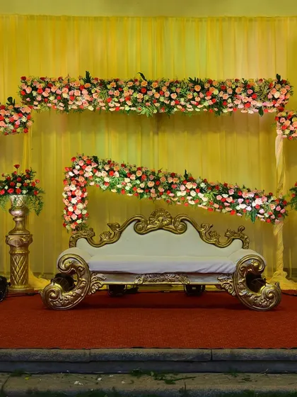 A classic reception stage with a floral arrangement that drapes beautifully over the couch. The combination of red, pink, and white flowers against a yellow backdrop is timeless.