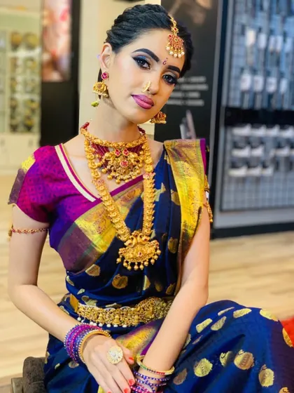 A full view of the South Indian bridal makeover, highlighting the beautiful contrast between the blue and purple saree and the heavy gold jewelry.