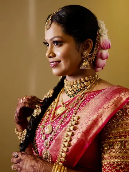 A side profile highlighting the beautiful braided hairstyle adorned with lotus flowers and the flawless finish of her makeup.