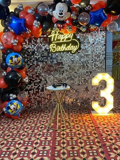 A classic Mickey Mouse theme for a 3rd birthday, featuring a silver shimmer wall, a red and black balloon arch with Mickey Mouse foil balloons, and a light-up number '3'.