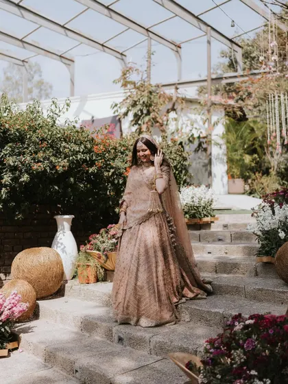 A bride descending the stone steps of the amphitheater, her beautiful lehenga trailing behind her, surrounded by flowers.