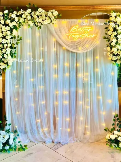 An elegant backdrop with a white floral frame and a 'Better Together' neon sign. The setup is clean, sophisticated, and perfect for Roka ceremonies or anniversaries.
