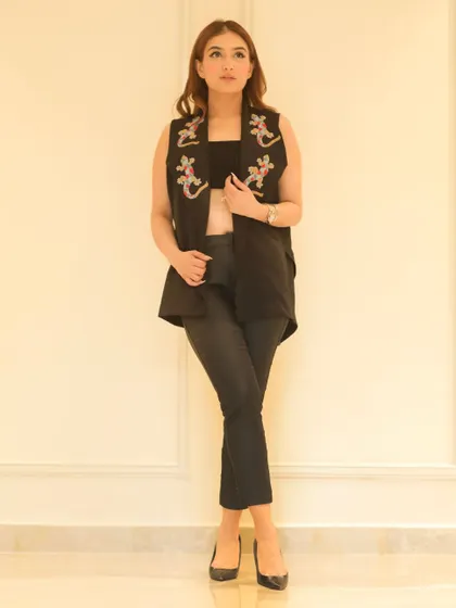 A model wearing a black embroidered vest over a crop top, showcasing a versatile piece for a fashion brand's collection.