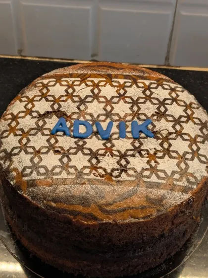 I love adding creative touches with powdered sugar stencils. This whole wheat cake features an intricate geometric pattern and a personalized name, showing how a simple dry cake can be beautifully decorated for a special person like Advik.