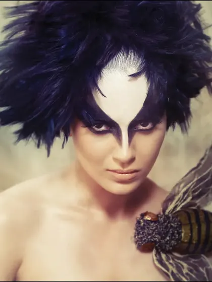 A conceptual beauty portrait of Kangana Ranaut. The dramatic, bird-like makeup and feathered hair transform her into a mythical creature, pushing the boundaries of conventional beauty.