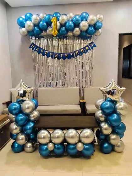 A classic birthday decoration for a home setting, with a silver shimmer curtain and balloon columns in metallic blue and silver.