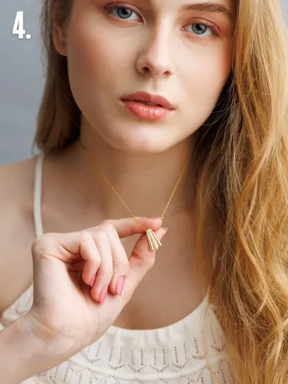 For delicate pieces like this gold pendant, we use soft, clean lighting to emphasize its form and finish. The model's gentle hold and the simple composition ensure the necklace remains the hero of the shot.