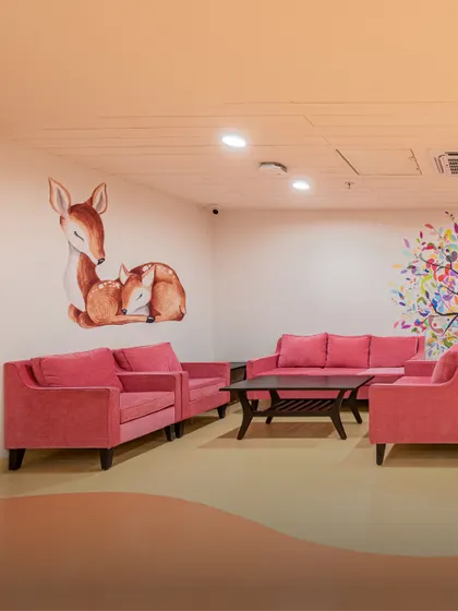 This waiting lounge for a pediatric or maternity ward uses soft pink sofas and a gentle deer mural. The design creates a warm, nurturing atmosphere for mothers, children, and families.