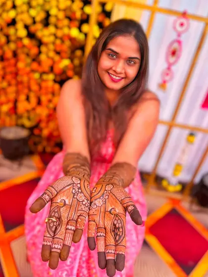 A happy bride showing off her beautiful wedding mehndi. The design features classic peacock motifs and delicate floral patterns, with a guaranteed dark stain from our natural henna.