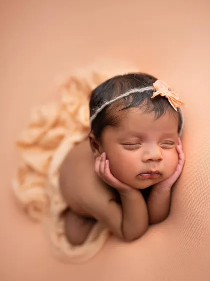 A wider view of the froggy pose, showing the baby's full form against a soft peach background.