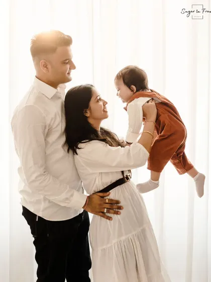 A light-filled family portrait celebrating a first birthday. The mother playfully lifts her child while the father looks on, creating a dynamic and joyful image.