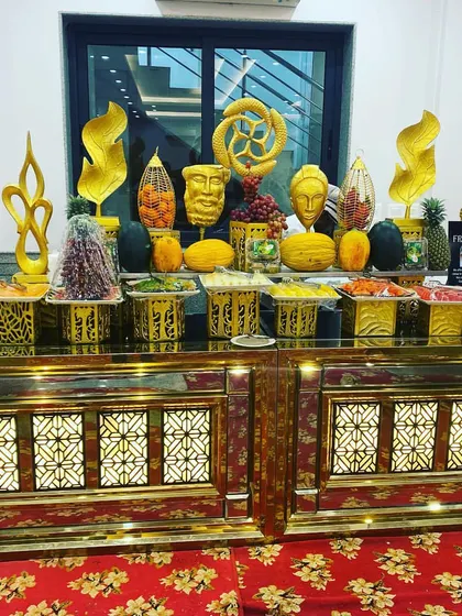 An exotic fresh fruit station set up for a luncheon. The counter features elaborate golden sculptures and a wide variety of local and imported fruits, creating a healthy and visually appealing option for guests.