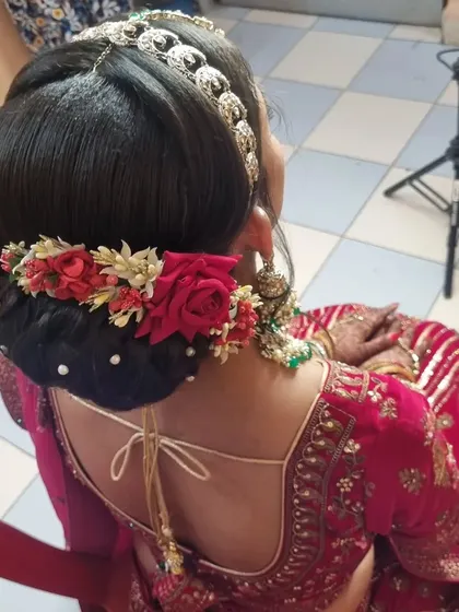 This bridal look features a beautiful red and green color combination. The hairstyle is a classic bun decorated with red roses and pearls, complementing her stunning lehenga.