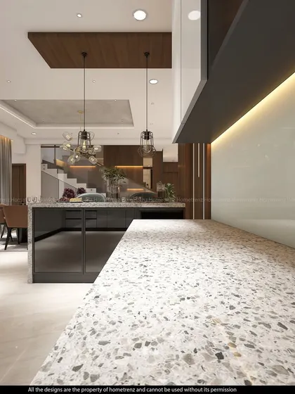 An open-plan kitchen with a large island featuring a terrazzo countertop. The design seamlessly connects the kitchen to the dining area, with pendant lighting defining the different zones.