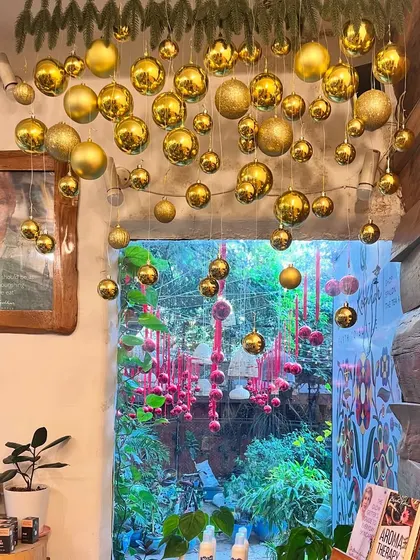 A glimpse from the inside out. The golden Christmas ornaments create a beautiful contrast with the lush greenery visible through the doorway, blending festive cheer with natural beauty.