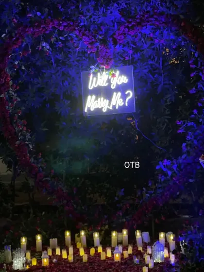 A wide view of an enchanting outdoor proposal setting at night. I used a large heart-shaped floral arrangement, a neon sign, and dozens of LED candles to create a warm, magical glow.