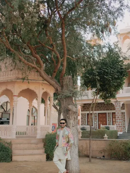 The groom looking cool and relaxed, leaning against a tree in the palace grounds during the Haldi festivities.