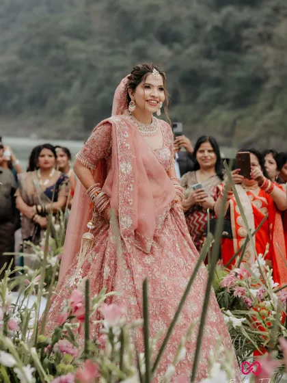 The bride's radiant smile as she makes her way to the mandap, walking through a path of flowers at her stunning riverside wedding.