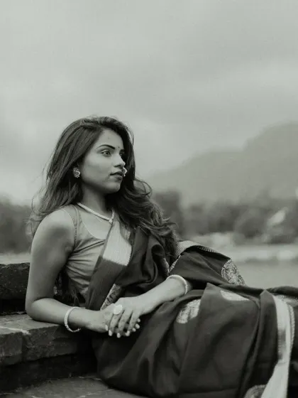 A pensive black and white portrait. The model is seated, looking out towards the horizon, with the landscape in the background adding a sense of scale and contemplation to the image.