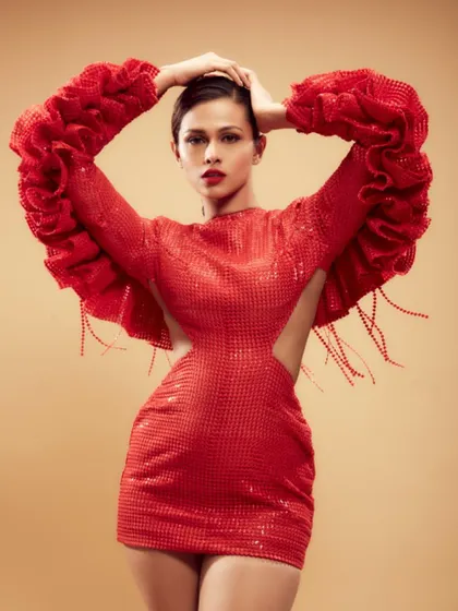 A full-length shot showcasing a powerful, high-fashion makeup look with a classic red lip. The makeup provides a strong focal point that complements the voluminous red gown, creating a cohesive and striking editorial image.