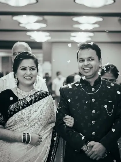 A timeless black and white photograph from an engagement ceremony. The couple makes their entrance, showered with petals by their loved ones, creating a classic and celebratory image.