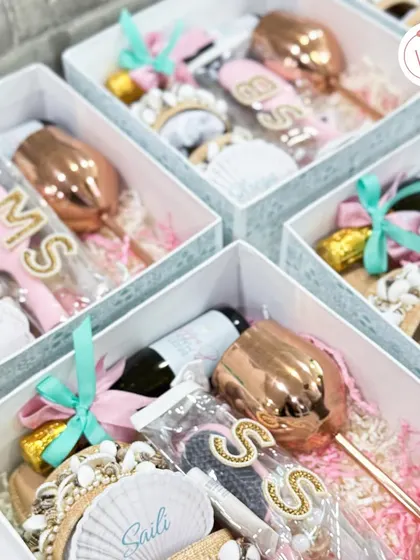 A collection of bridesmaid proposal boxes, each personalized with initials and filled with goodies like custom wine glasses and beach-ready accessories.