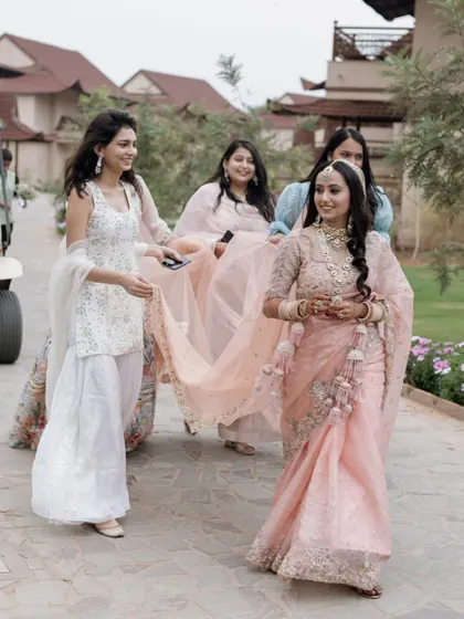 A candid moment of the bride walking with her bridesmaids, who are helping carry her long, flowing dupatta.